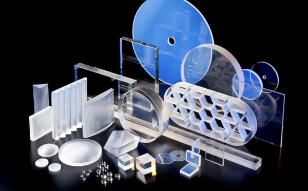 A spread of precision optics on black: lenses, prisms, windows, cubes and coated plates